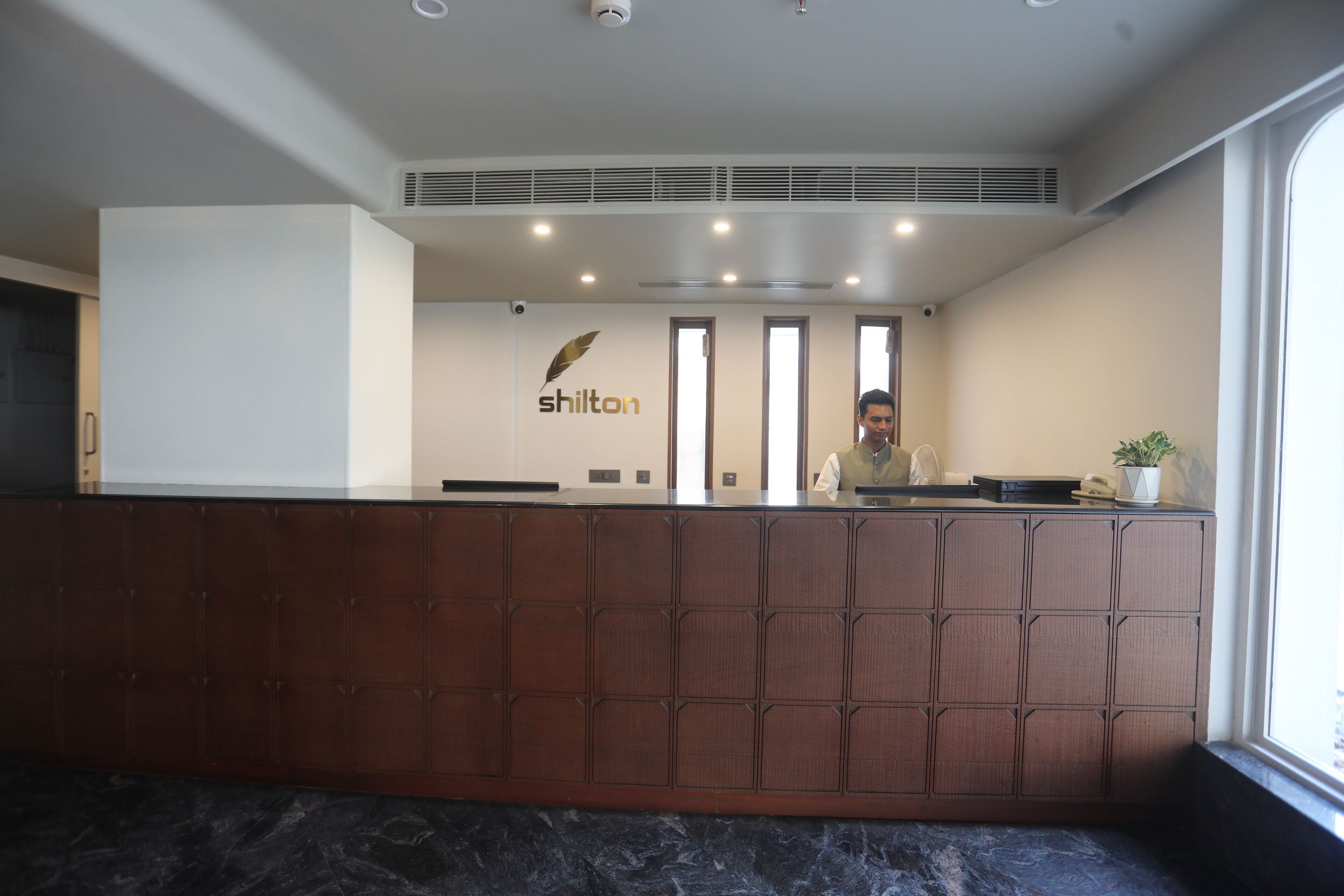 A reception desk with a logo, a plant, and a window.