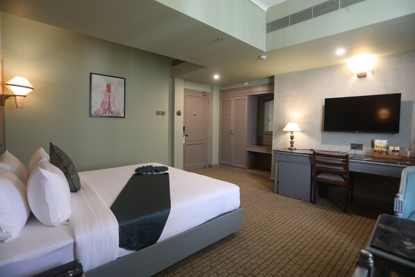 A hotel room with a bed, desk, chair, TV, and a door leading to a bathroom. - Shilton International (Kanayannur)