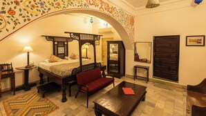 Quarto tradicional com cama de dossel, um sofá vermelho, uma mesa de centro de madeira e um tapete estampado.