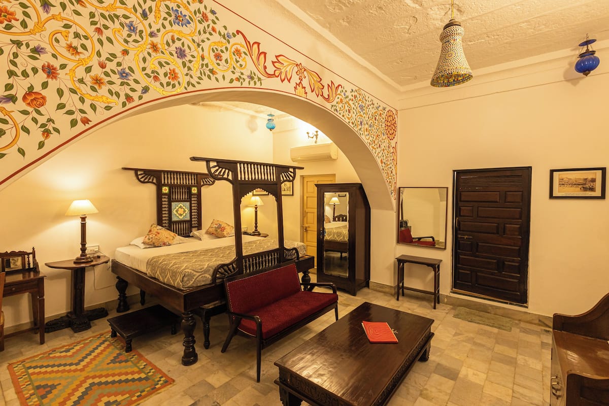 A traditional room with a four-poster bed, a red sofa, a wooden coffee table, and a patterned rug.