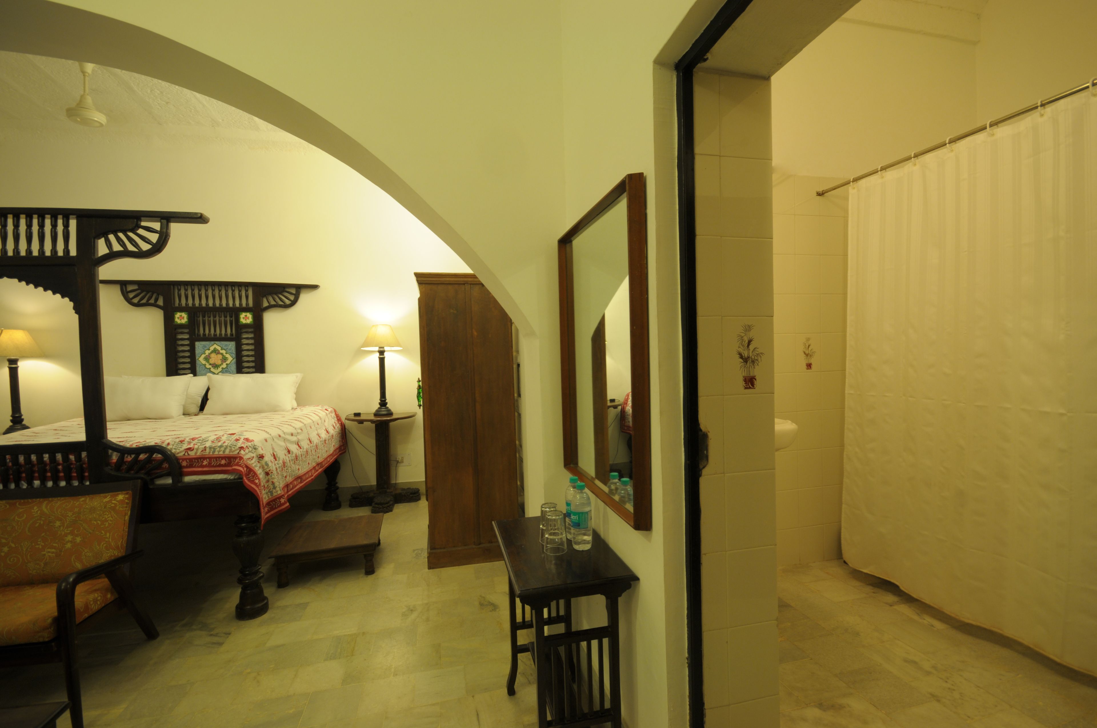 Un dormitorio con cama, mesita de noche, lámpara y espejo.
