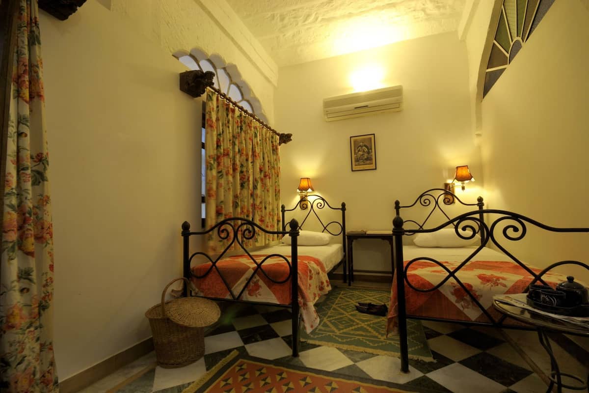 A room with two beds, a checkered floor, a wall-mounted air conditioner, and a small table with a lamp.