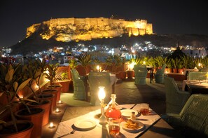 Un área de comedor al aire libre con macetas de terracota, una mesa preparada para dos personas y una vista de una fortaleza histórica al fondo.