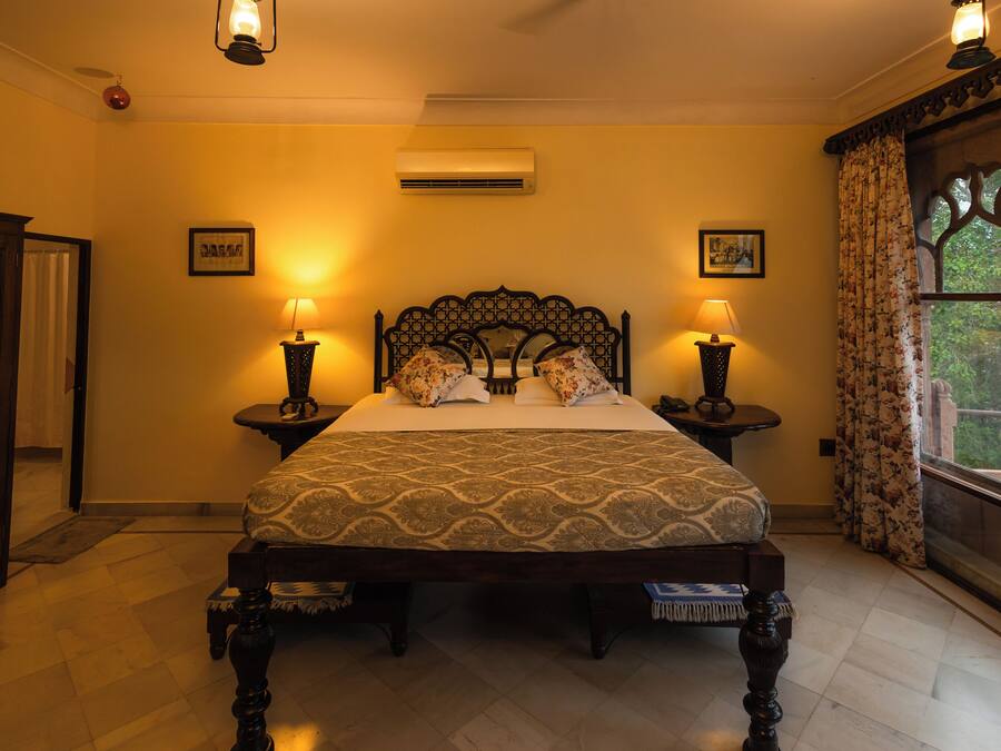 A neatly made bed with a patterned bedspread, two bedside lamps, and a window with curtains.