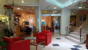A modern lobby with red sofas, a glass coffee table, and potted plants.