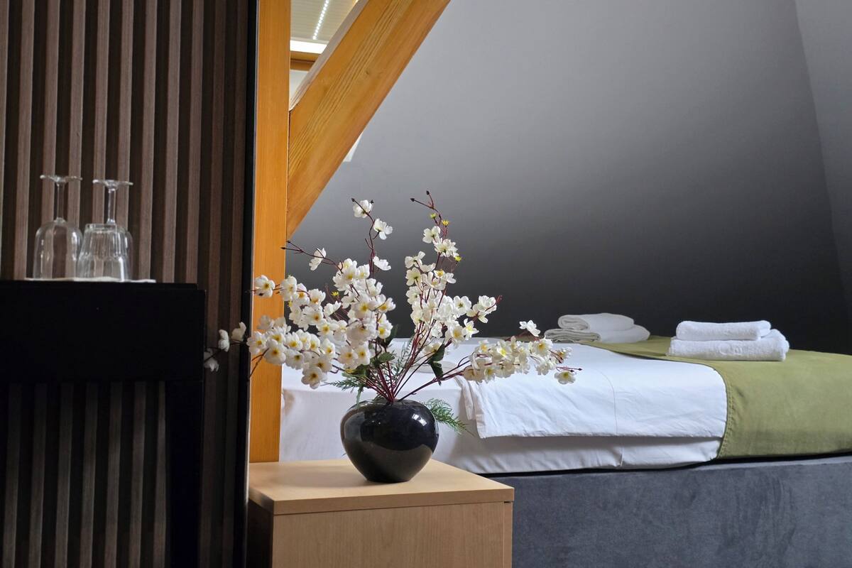 Un dormitorio con cama, una mesita de noche con un florero y un cabecero de madera.
