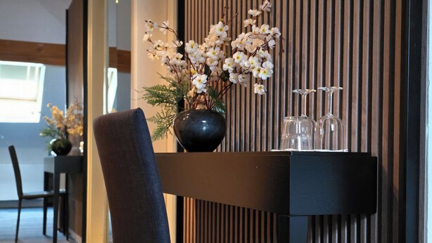 A modern dining area with a dark wooden table, a vase of white flowers, and a chair.