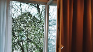 A room with a bed, a white chair, and a view of trees through a window.