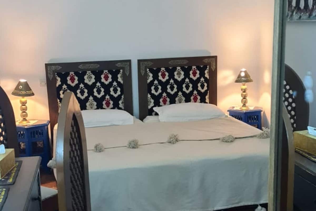 A bedroom with a bed, two bedside lamps, a chair, a desk, and a patterned rug.
