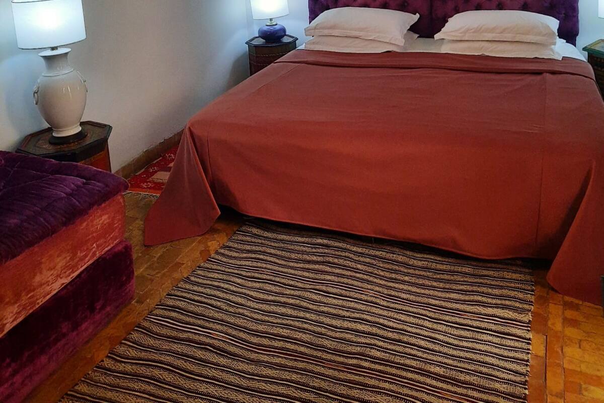 A bedroom with a bed, two bedside tables, a rug, and a wall-mounted artwork.