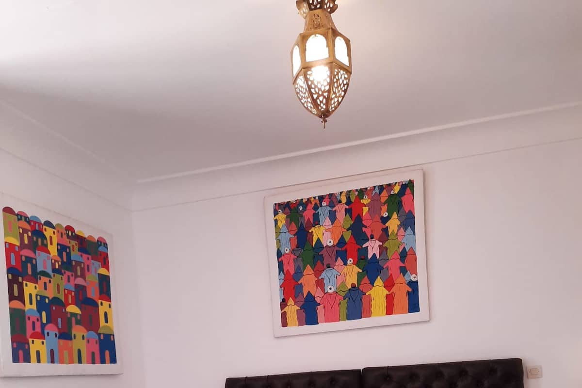 A bedroom with a bed, two nightstands, a lamp, and two wall art pieces.
