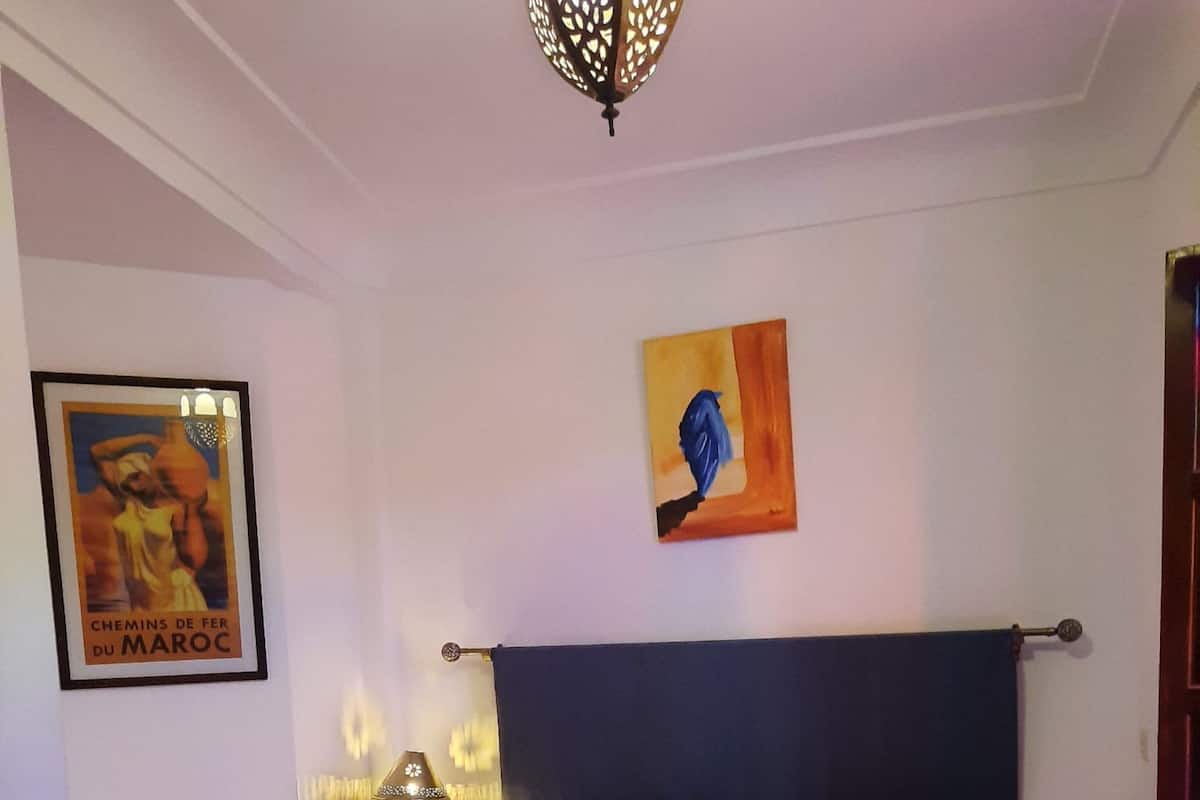 A bedroom with a bed, a nightstand, a lamp, a framed picture, and a ceiling light.