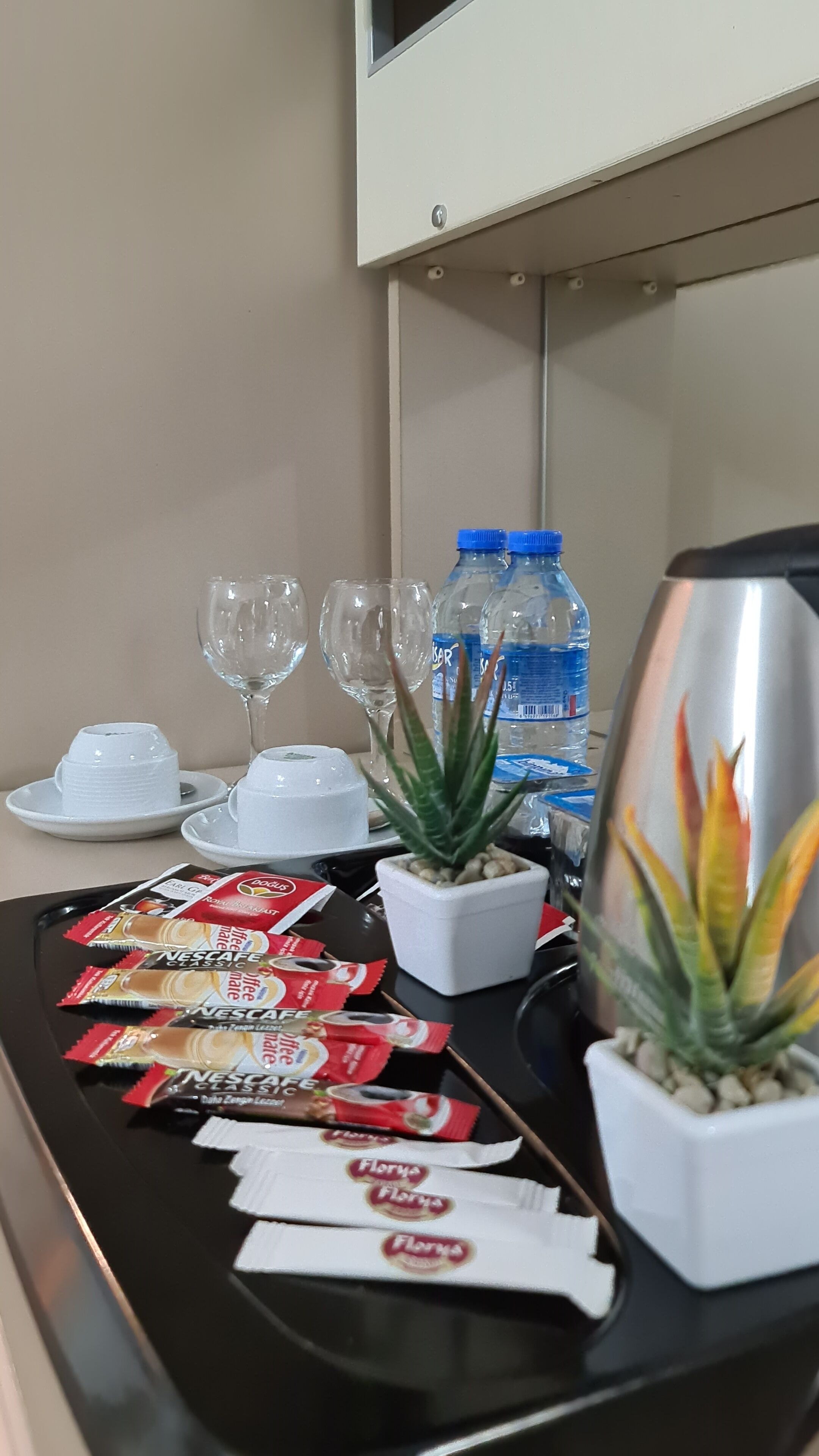 A hotel reception area with a coffee station, water bottles, and a small plant.