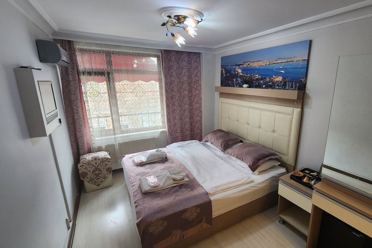 A bedroom with a bed, a nightstand, a TV, and a window with curtains.