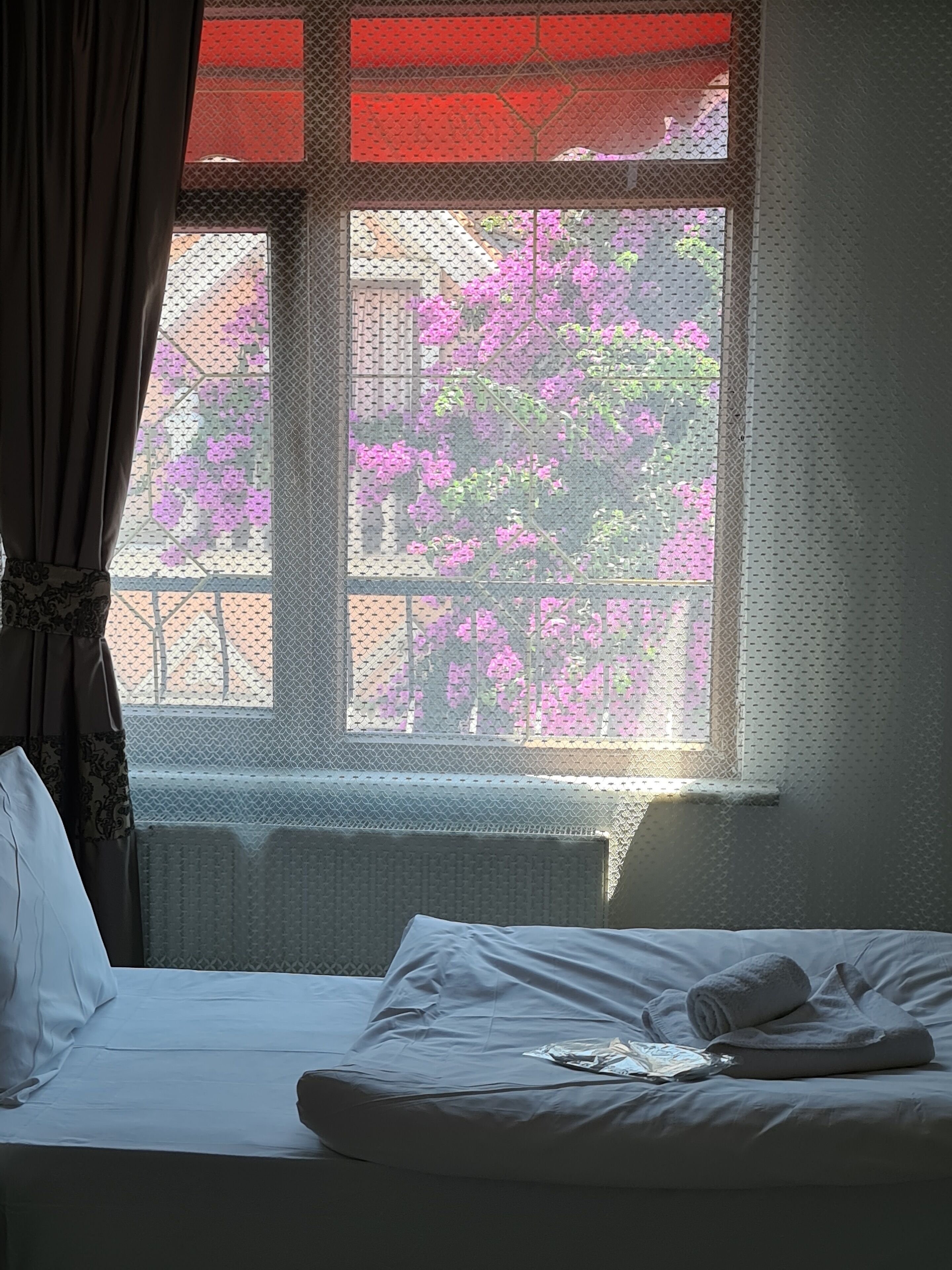 A bedroom with a bed, a window with a view of pink flowers, and a curtain.
