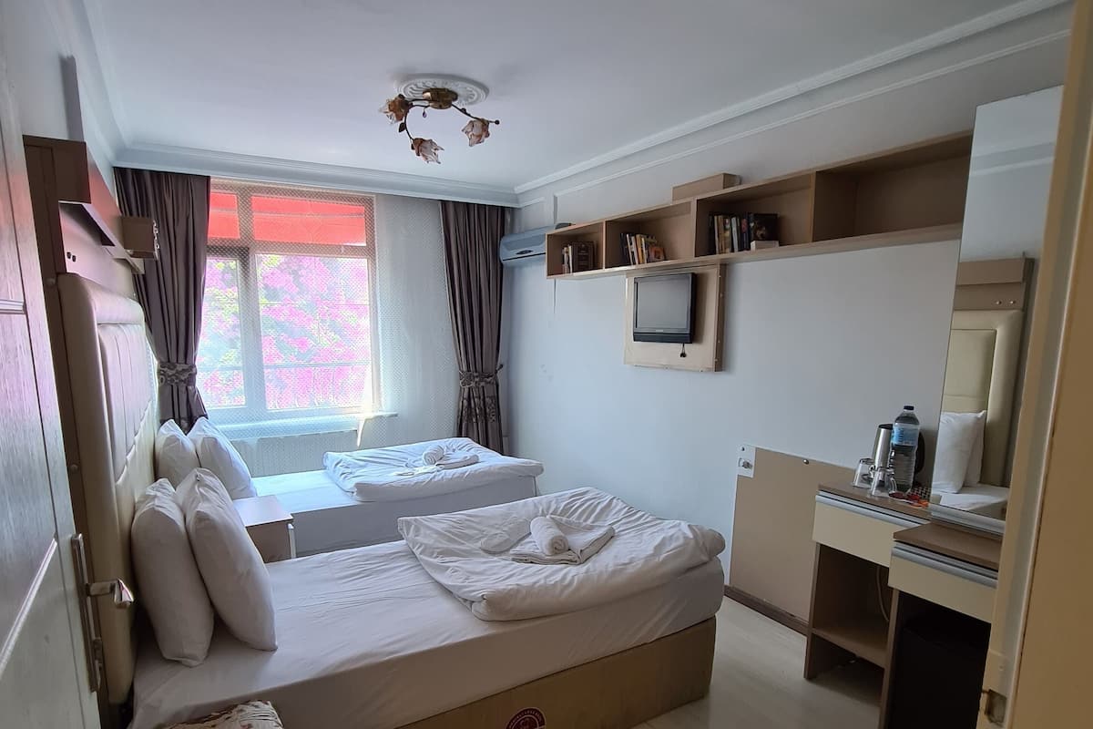 A hotel room with two beds, a desk, a TV, and a window with curtains.