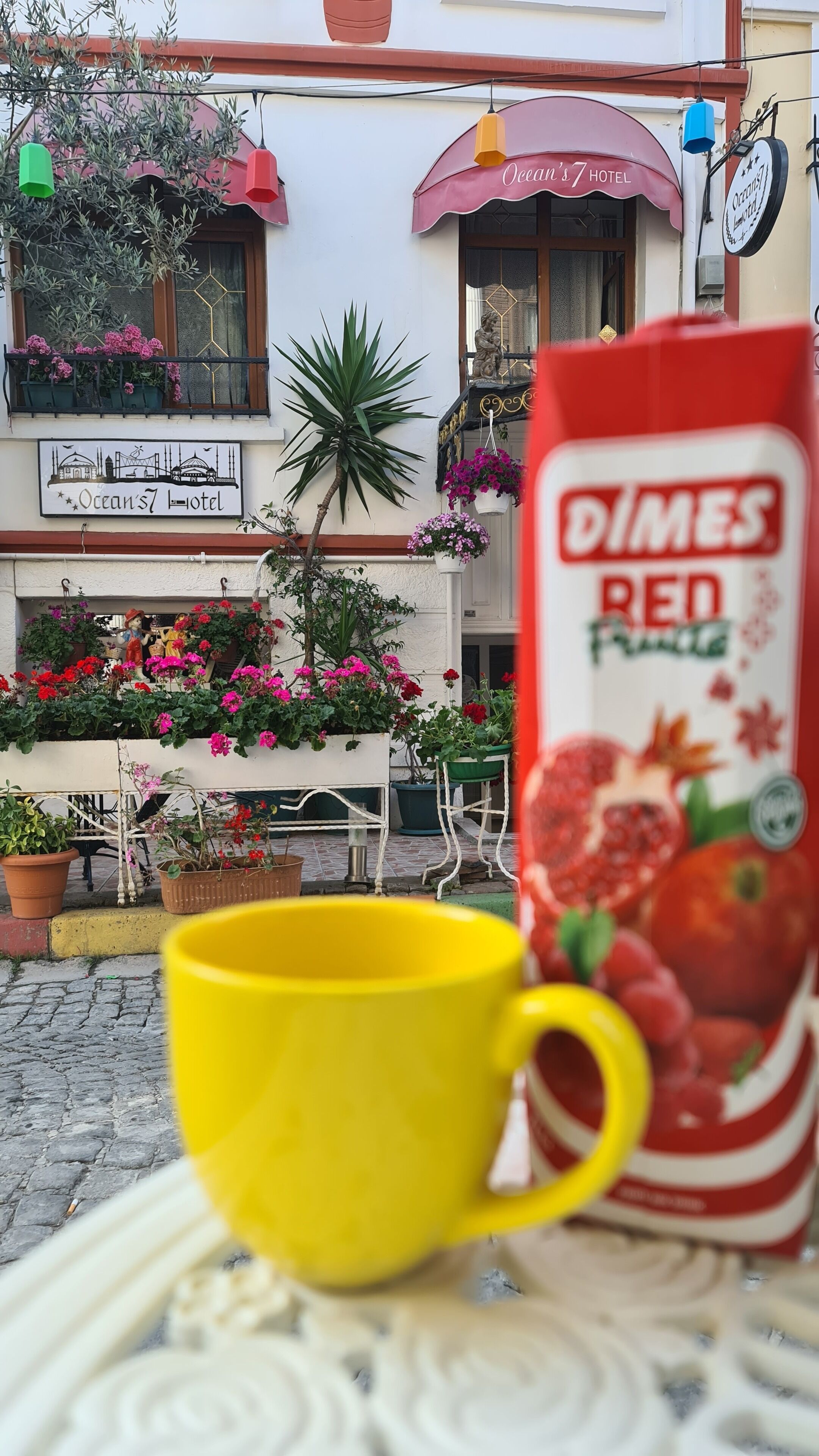 A yellow cup on a table in front of a building with a sign for Ocean's 7 Hotel.
