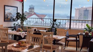 A dining area with tables and chairs, a view of buildings and a bridge, and a balcony with a railing. - Oceans 7 Hotel  (Istanbul)