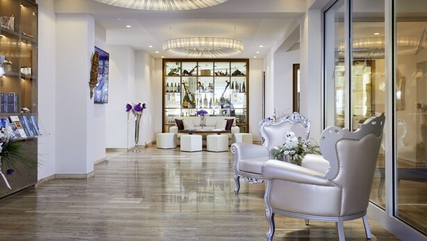A spacious lobby with a wooden floor, elegant white furniture, and a glass display case filled with bottles. - Hotel Barbarahof Kaprun -  Adults Only (Kaprun)