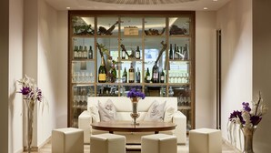 A modern lounge area with a glass display case of wine bottles, a white sofa, and a round table with matching ottomans. - Hotel Barbarahof Kaprun -  Adults Only (Kaprun)