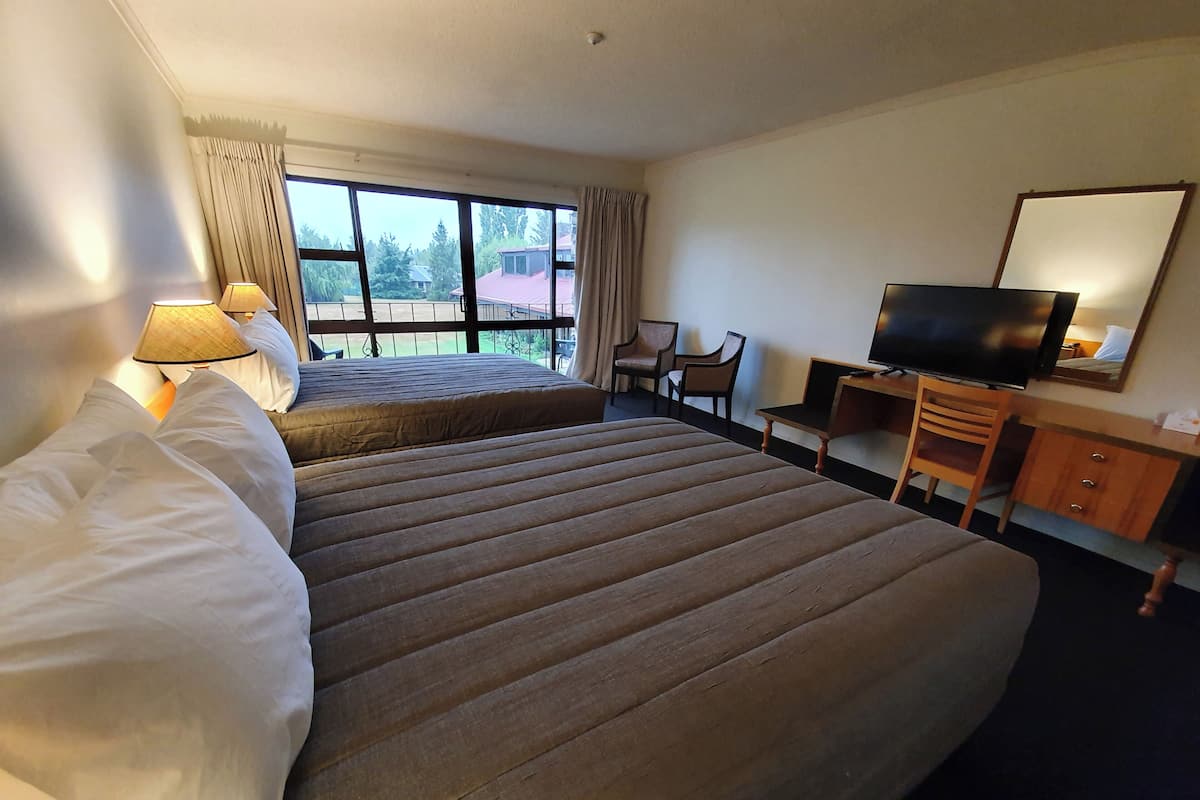Habitación de hotel con una cama grande, un escritorio con televisor y vistas al exterior.