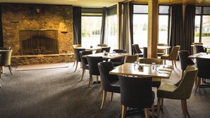 A restaurant with a stone fireplace, large windows, and modern furniture. - Distinction Mackenzie Country Hotel (Twizel)