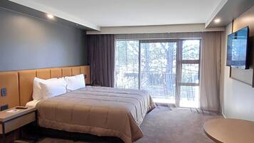 Une chambre d’hôtel avec un grand lit, une table de chevet, un téléviseur fixé au mur et une vue sur les arbres par la fenêtre.