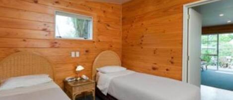 A room with two beds, wooden walls, a small table with a lamp, and a window.