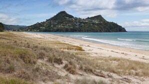 Una playa con una colina al fondo, una orilla arenosa y un cielo despejado.