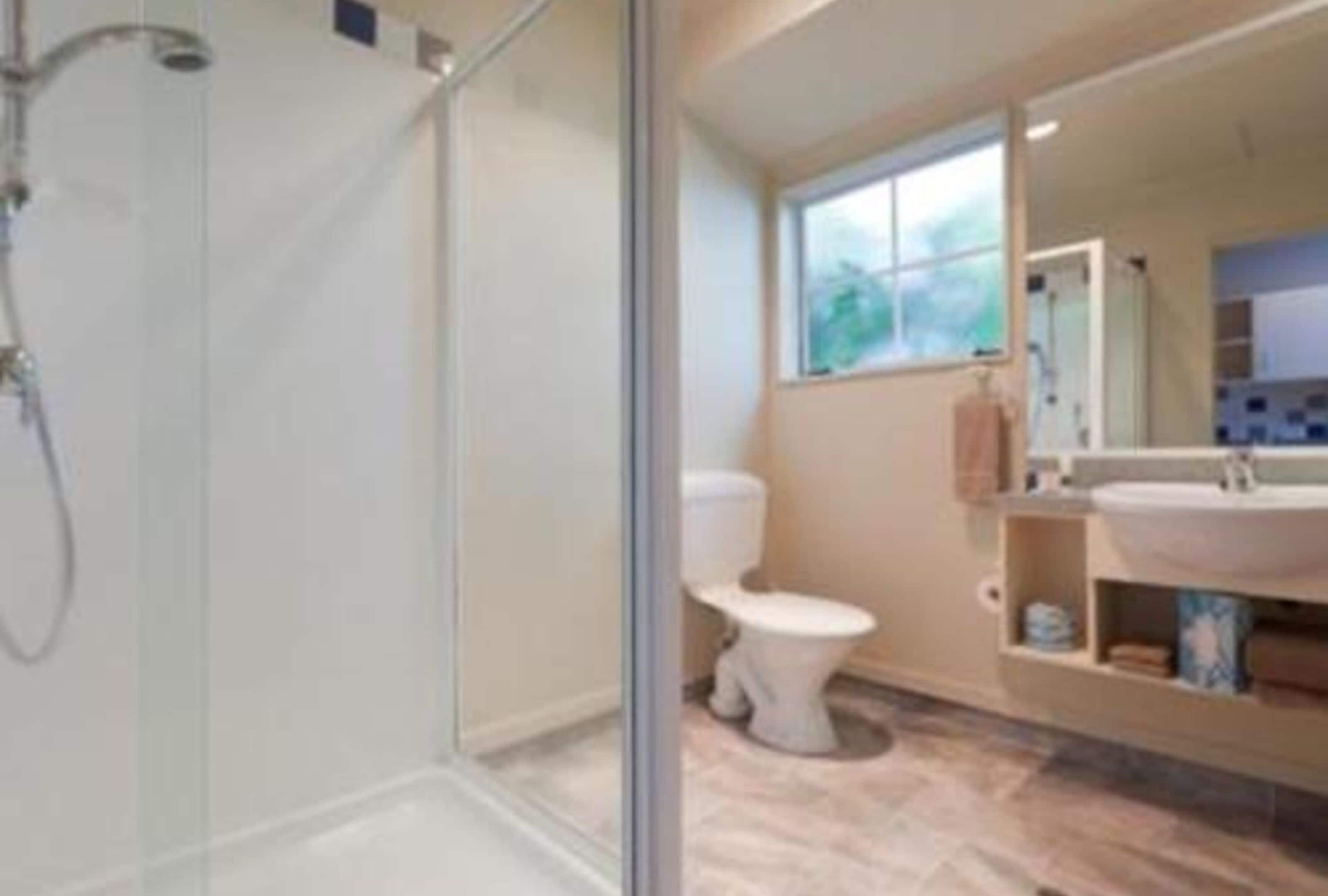 A modern bathroom with a glass shower enclosure, a toilet, and a vanity with a sink and mirror.