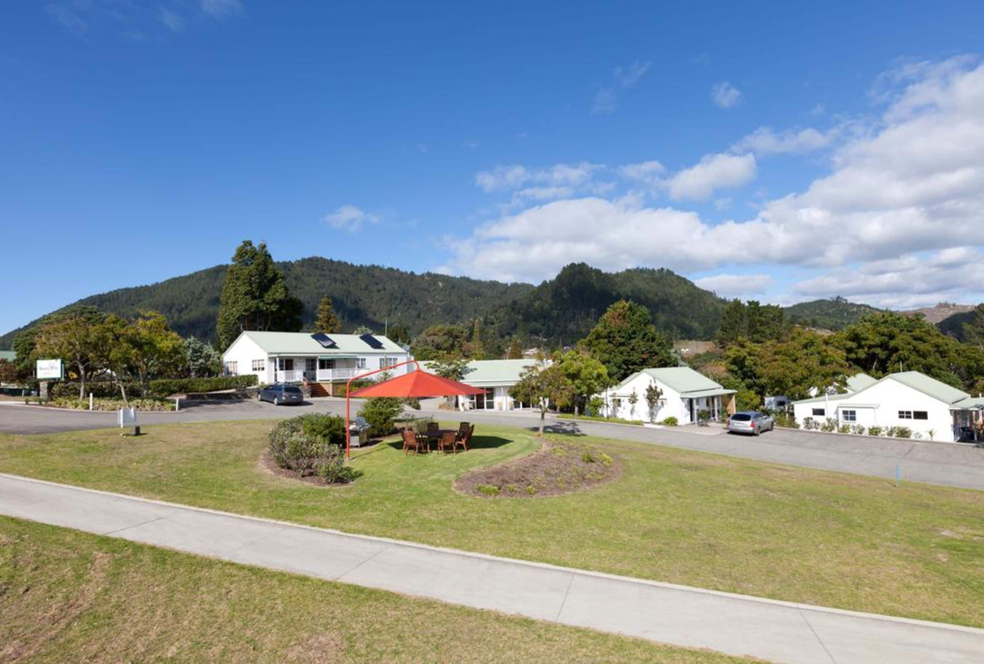 A hotel with a red-roofed building, a grassy lawn, and a mountain backdrop.