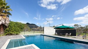 Una piscina con cubierta de madera, rodeada de vegetación y una montaña al fondo.