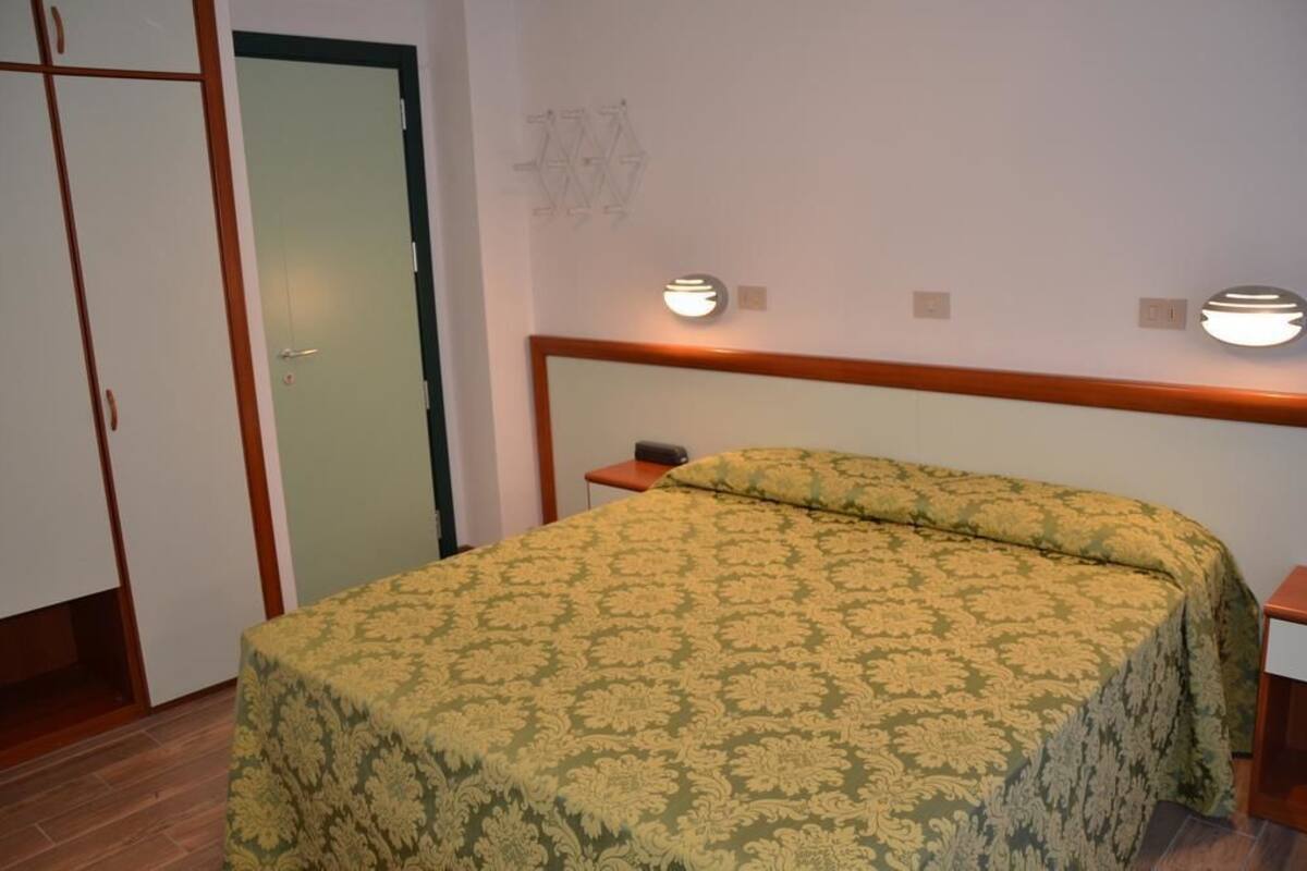 A bedroom with a bed, a wardrobe, and two wall-mounted lights.