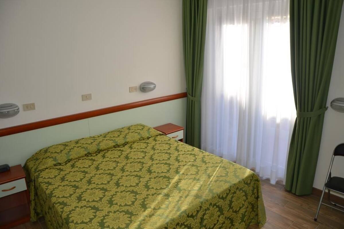 A hotel room with a bed, a nightstand, a chair, and a window with curtains.