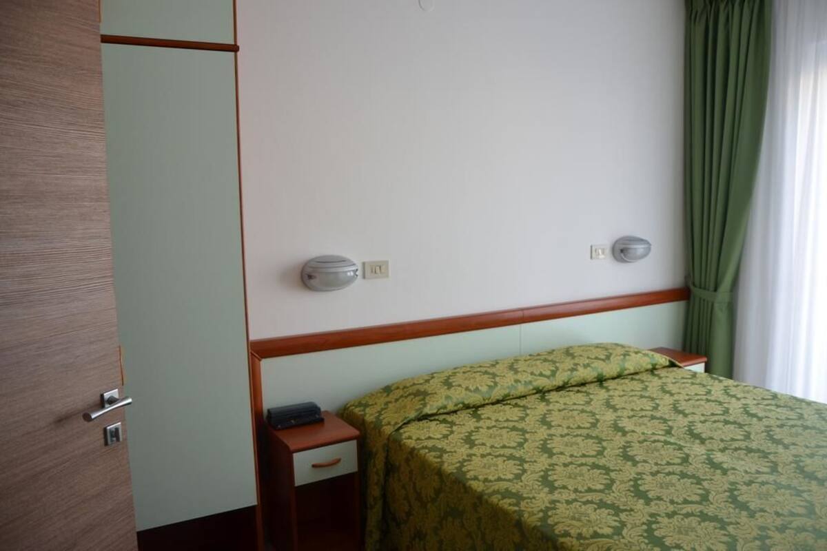 A hotel room with a bed, a nightstand, a wooden wardrobe, and a green curtain.