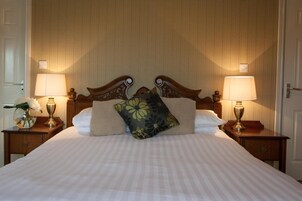 Una cama bien tendida con almohadillas florales, dos lámparas de noche y un jarrón con flores sobre una mesita de noche.