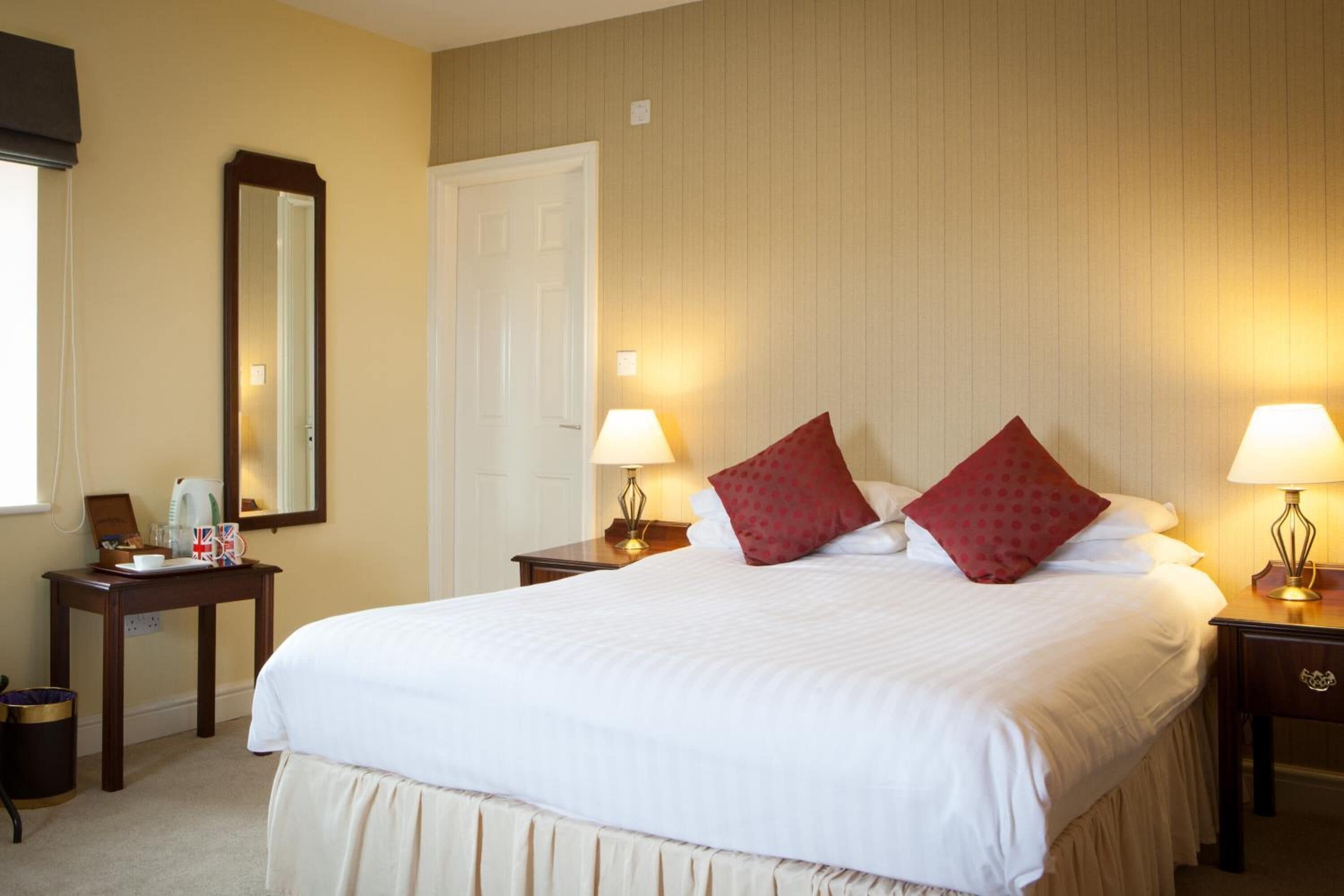 A neatly arranged hotel room with a large bed, two bedside tables with lamps, a bedside mirror, and a small table with a tray.