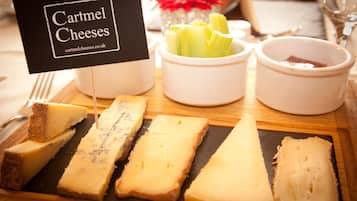 A cheese board with various types of cheese, celery, and a small sign that reads "Cartmel Cheeses."