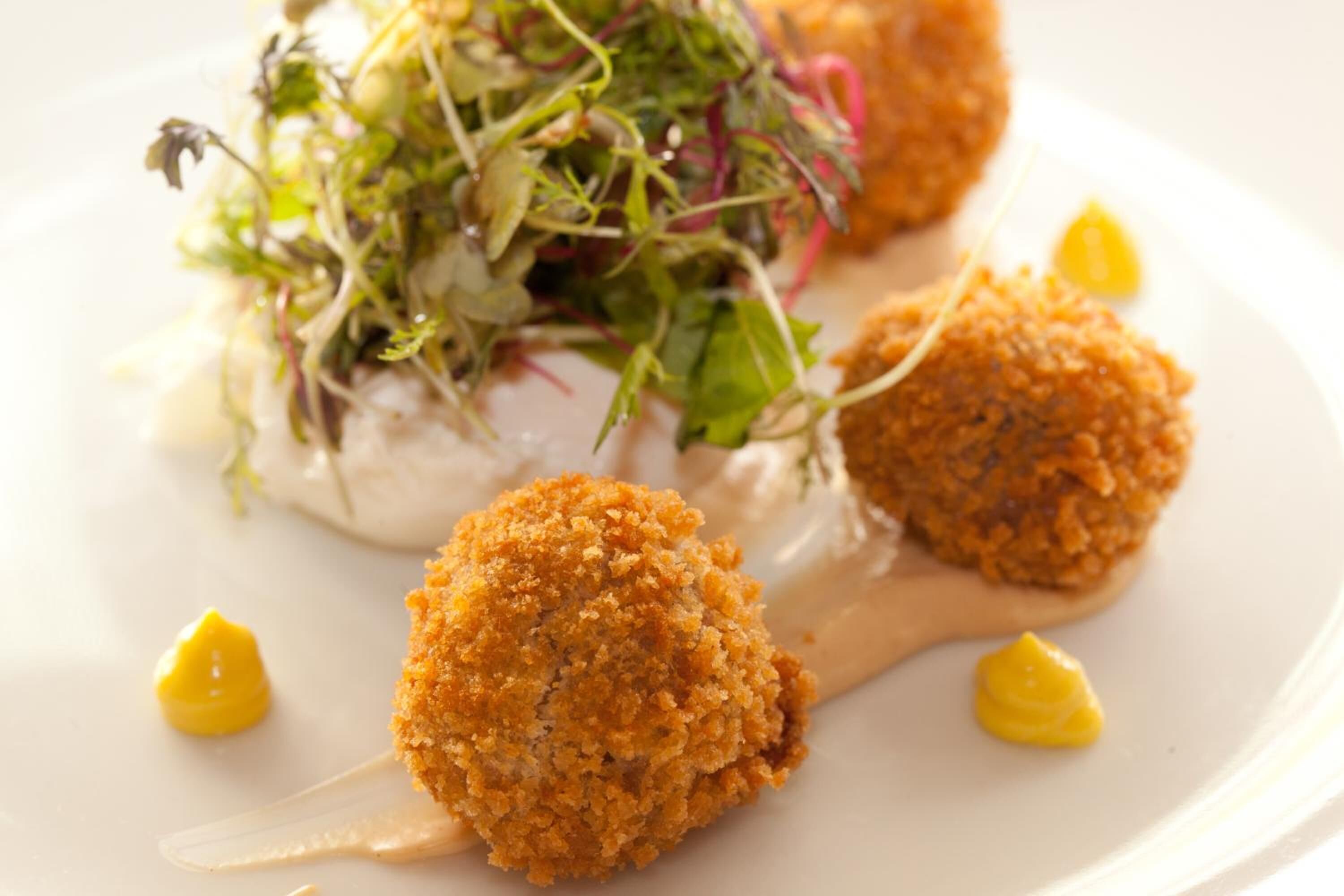 Une assiette contenant trois boulettes panées, une salade et une sauce crémeuse.