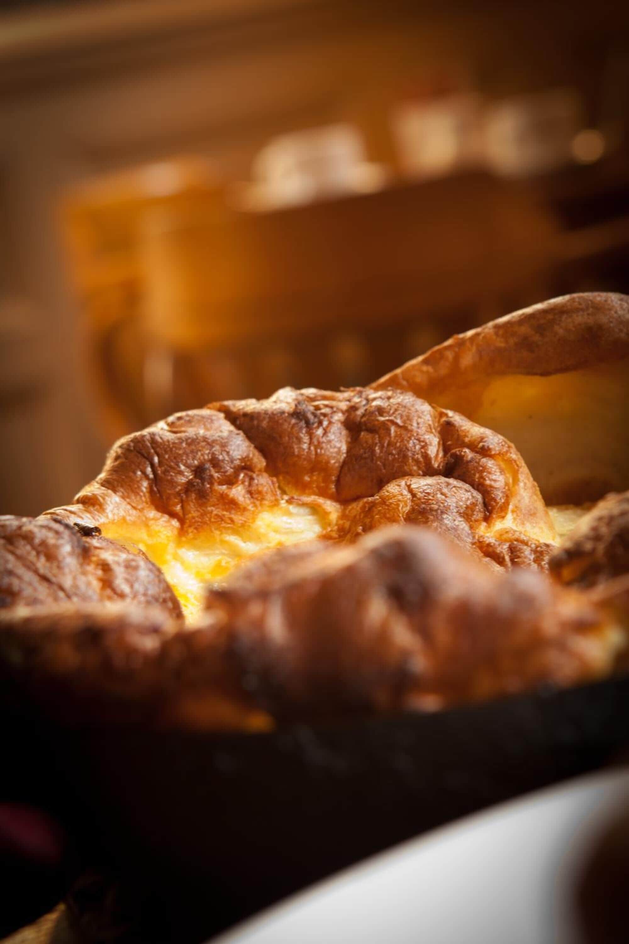 A close-up of a baked dish with a golden-brown crust, possibly a savory pie or tart, in a black baking dish.