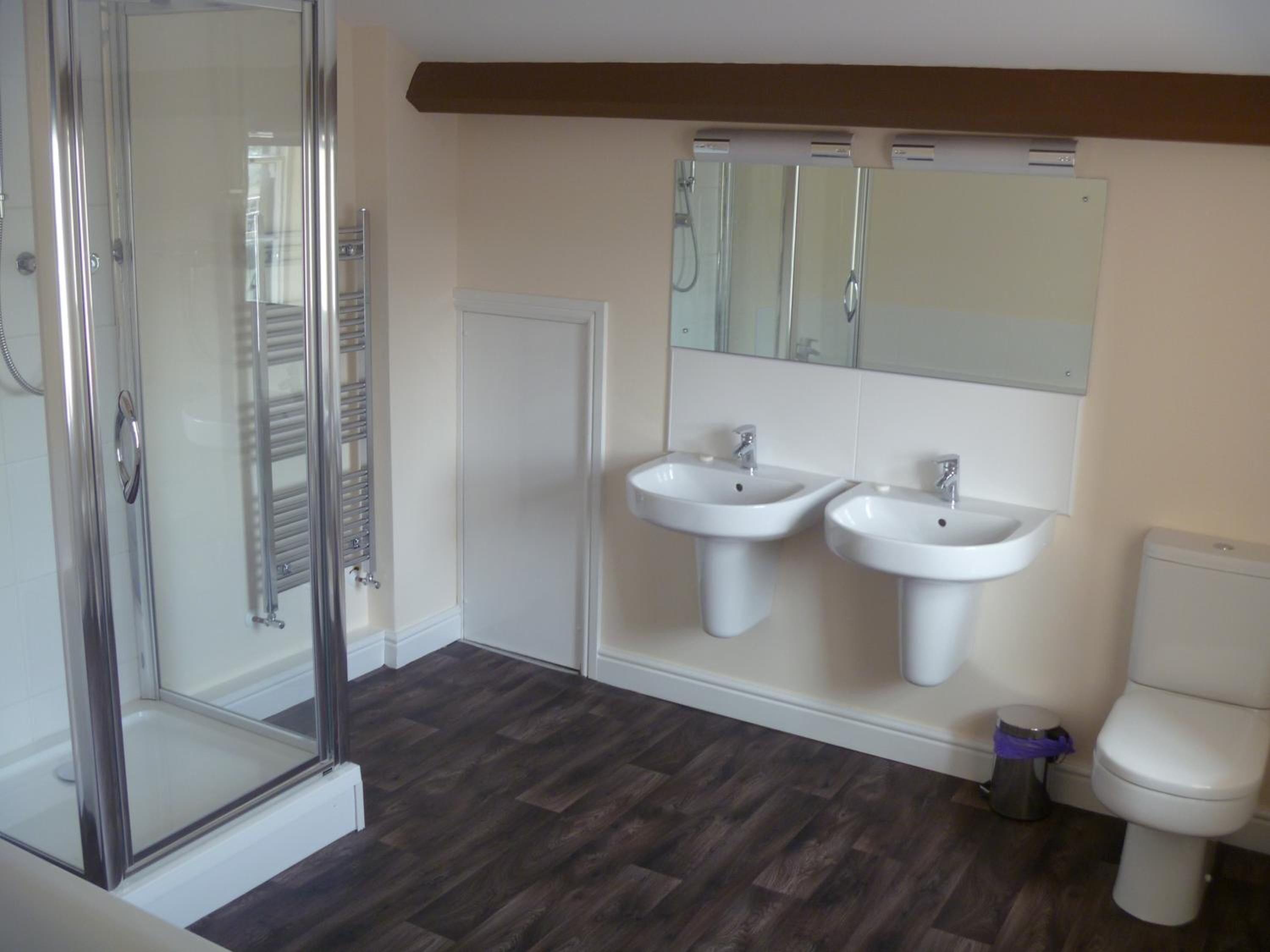 A bathroom with a glass shower enclosure, two sinks, a toilet, and a mirror above the sinks.
