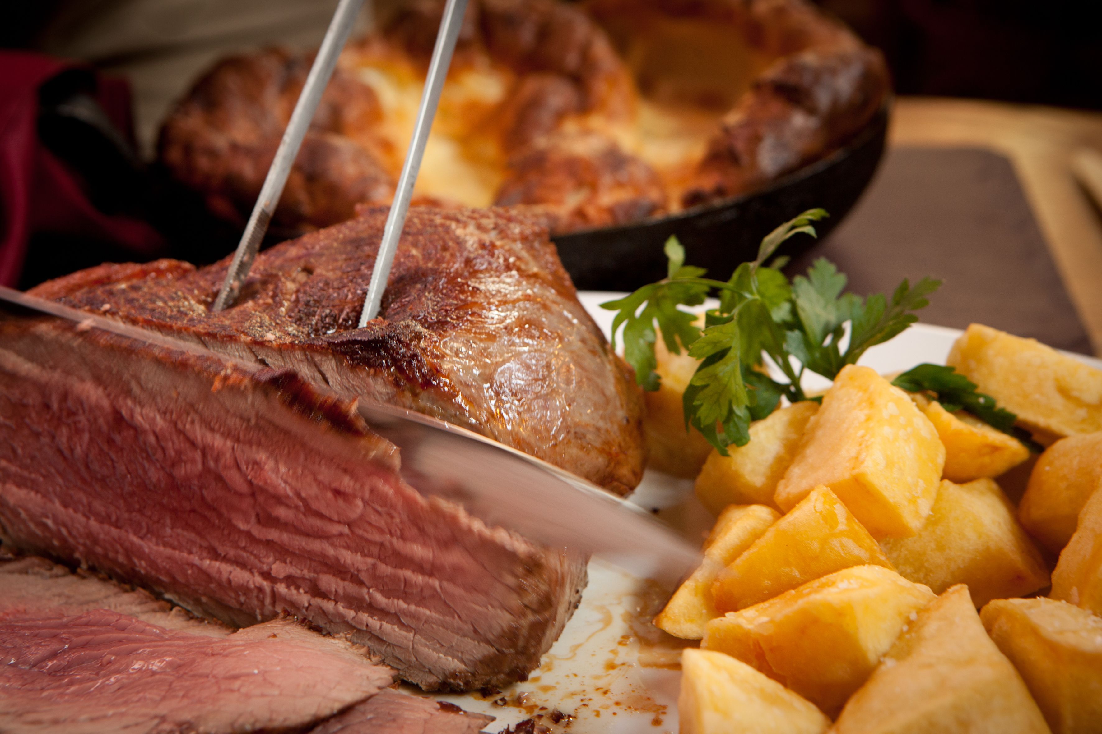 A steak with a fork and knife, accompanied by roasted potatoes and a garnish of parsley.