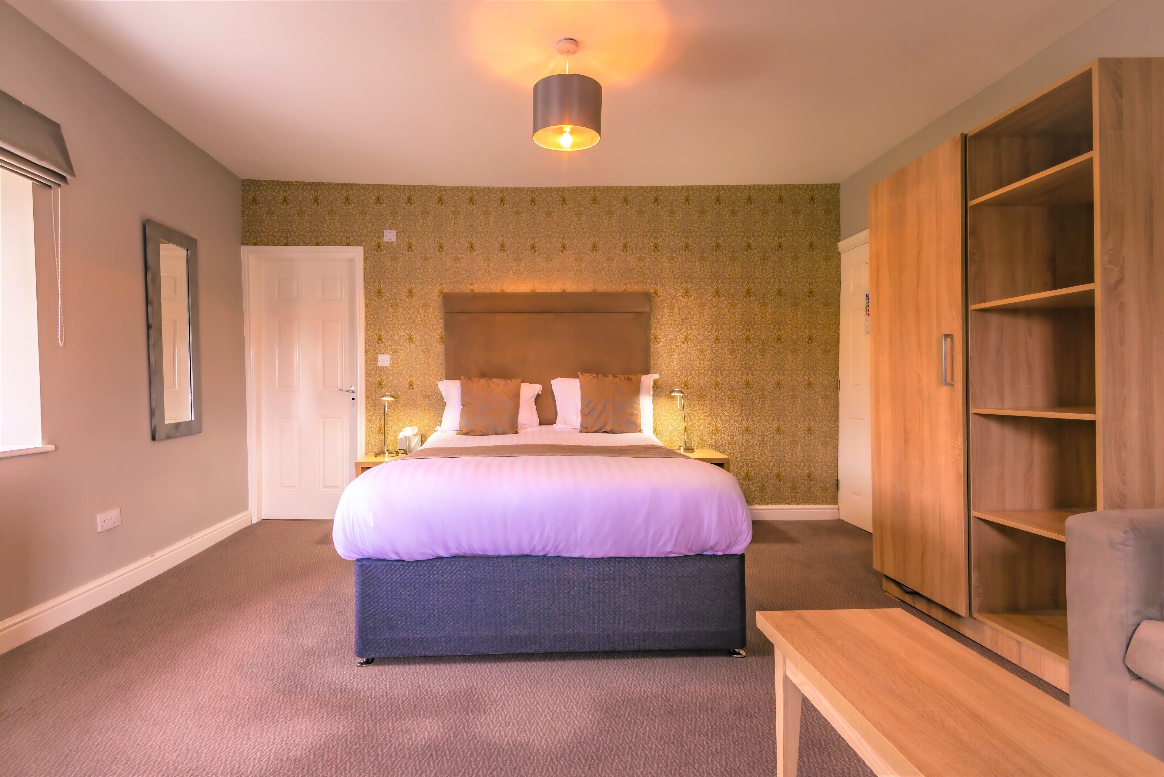 Une chambre  à coucher avec un grand lit, une armoire, une table de chevet et une lampe.