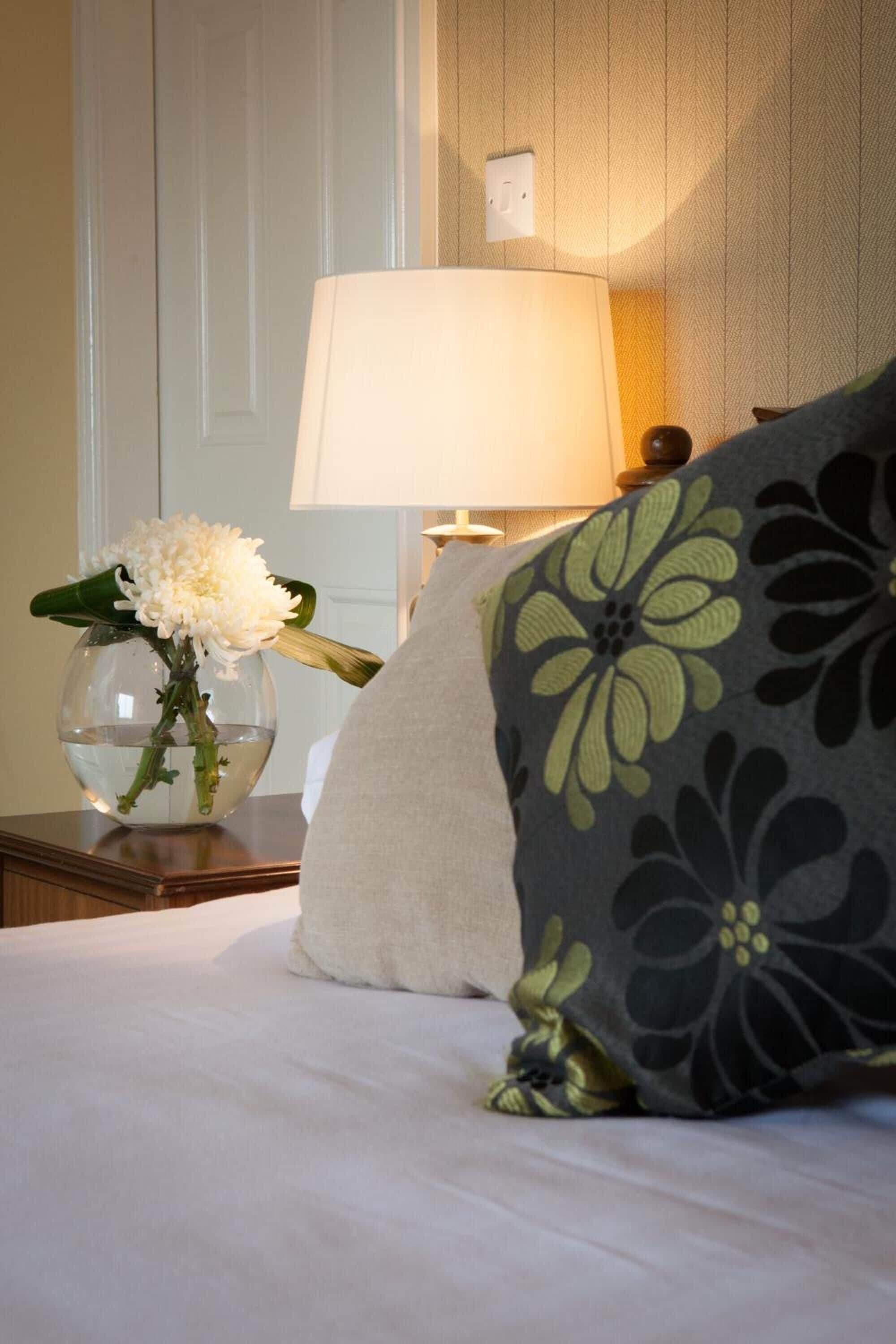 A neatly made bed with a pillow and a vase of flowers on a bedside table.