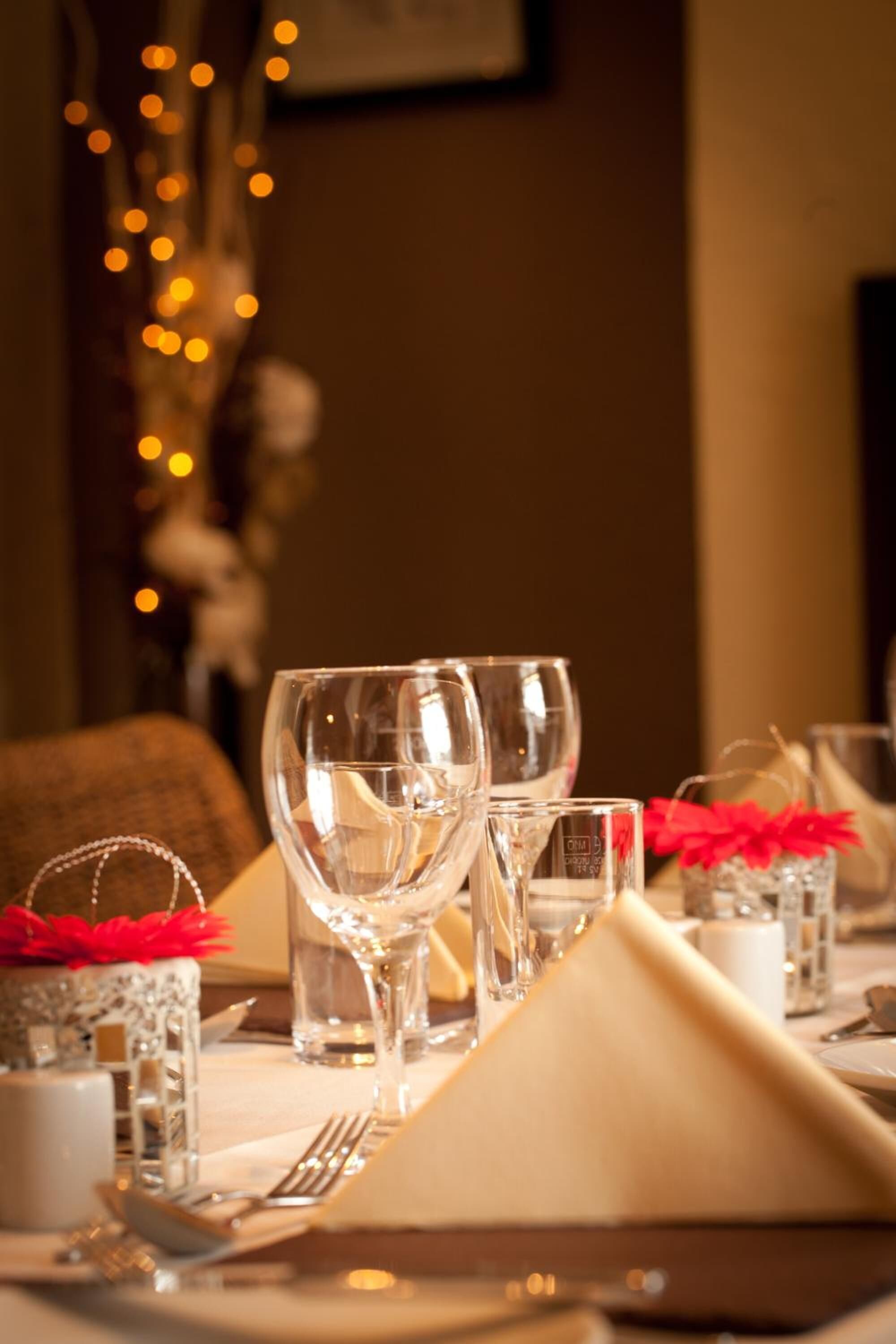 A dining table set with clear glassware, a folded beige napkin, and small glass containers with red decorations.