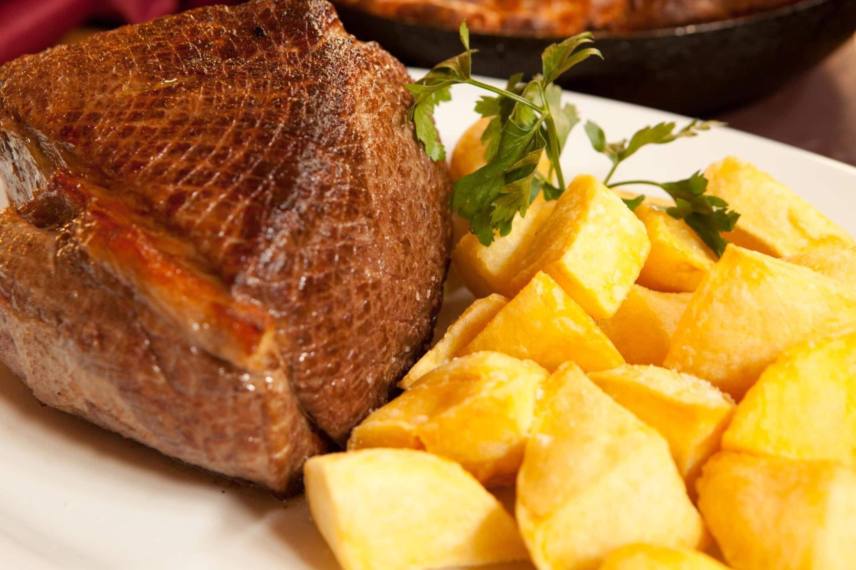 Une assiette contenant de la viande cuite et des morceaux de fruit jaune, probablement de la mangue, le tout garni d’herbes vertes.