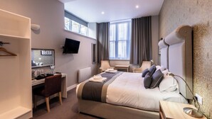 Habitació d'hotel amb llit, escriptori, cadira, televisió i grans finestres.