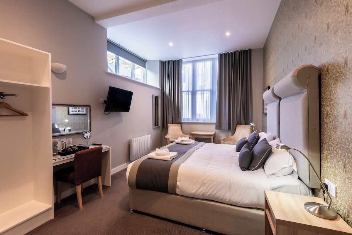Habitación de hotel con cama, escritorio, silla, televisor y ventanas amplias.