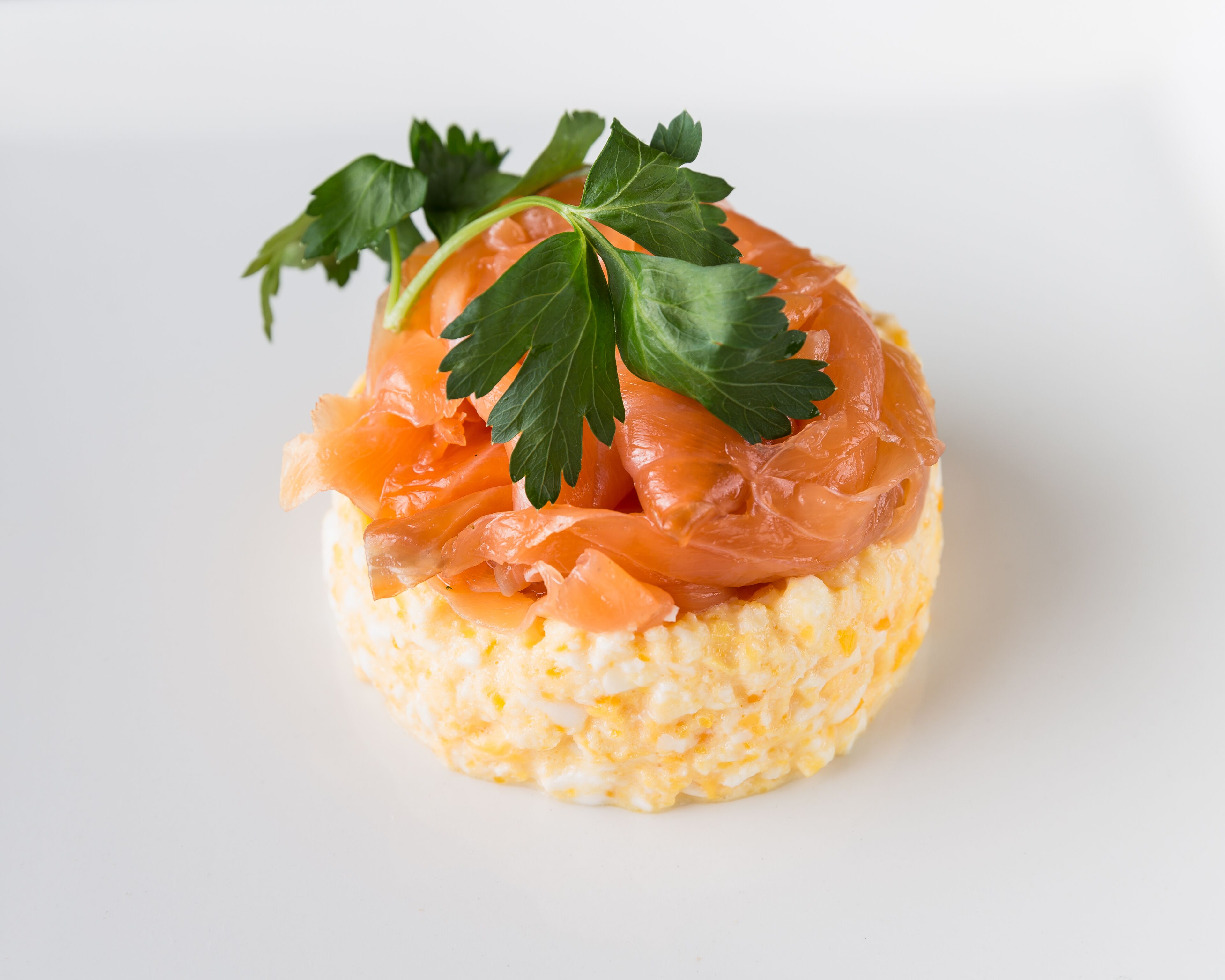 A small round dish with a base of what appears to be a creamy mixture, topped with slices of smoked salmon and garnished with a sprig of parsley.