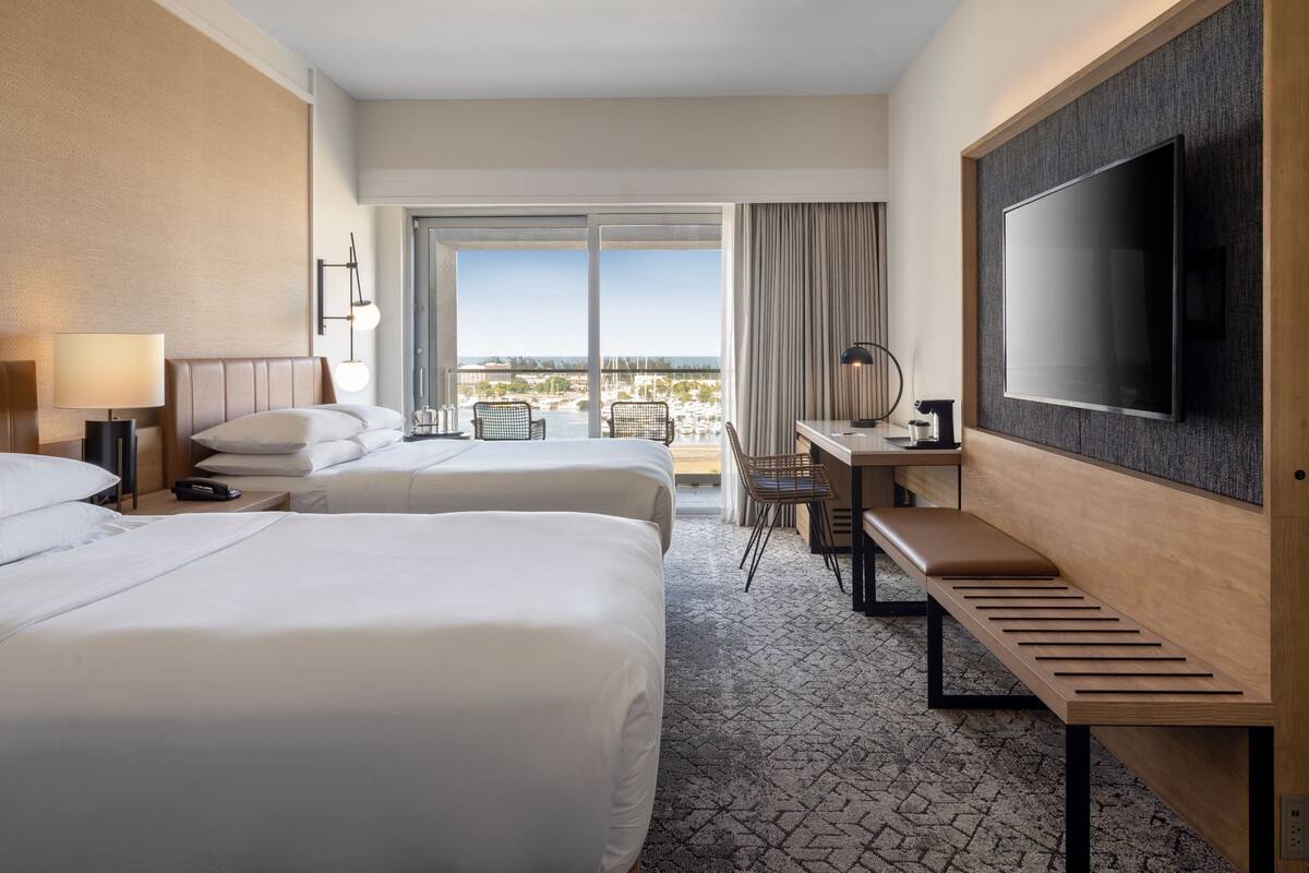 Une chambre d’hôtel avec deux lits, un bureau, une télévision et un balcon avec vue.